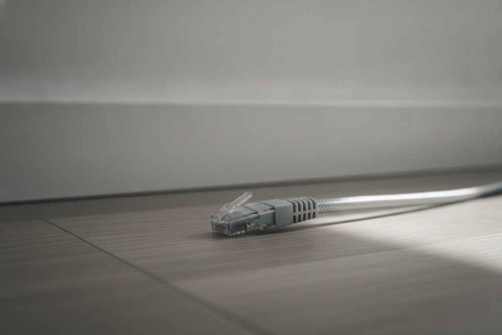 Câble Ethernet gris courant le long d'une plinthe blanche au ras d'un parquet clair